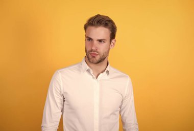 Beyaz tişörtlü yakışıklı adam turuncu arka planda duruyor, iş modasında.