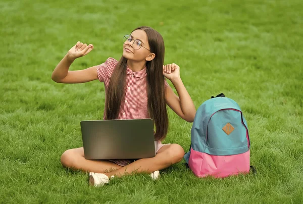 Tempo libero. Torniamo a scuola. educazione online. giorno della conoscenza. lezione privata per bambini. blogging. ragazza spensierata seduta su erba verde con computer portatile. Inizia. bambino giocare al gioco per computer — Foto Stock