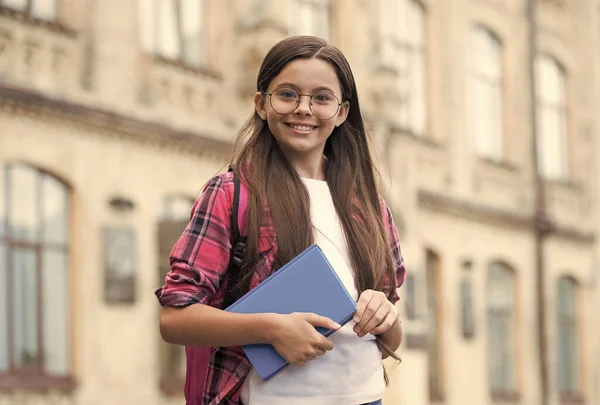 Criança feliz com olhar inteligente segurar livro de leitura em estilo de moda casual ao ar livre, de volta à escola — Fotografia de Stock