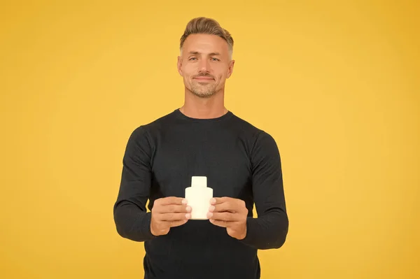 Hombre caucásico guapo con la piel de la cara sin afeitar y el pelo elegante en estilo casual celebrar perfume botella fondo amarillo, cuidado de la piel —  Fotos de Stock