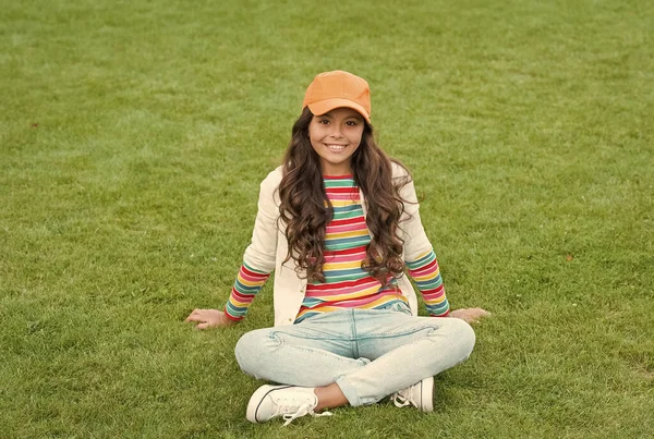 Poserar för foto. vacker student tonåring flicka i parken. söt leende säker skolflicka koppla av på grönt gräs. Lycklig barndom. Tillbaka till skolan. Liten flicka bär avslappnade kläder. skönhet och mode — Stockfoto