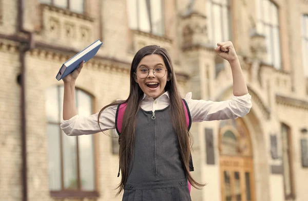 Happy kid show power hand gesture holding school book outdoors, knowledge — Stock fotografie