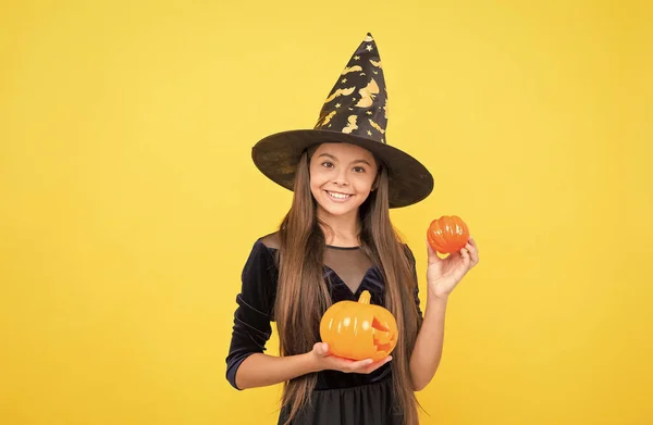 Halloweeni boszorkány lány. Boldog gyermekkort. tinédzser gyerek boszorkánykalapban. Vidám gyerek kezében tök. Karnevál jelmezbál. Csokit vagy csalunk. Ünnepelni az ünnepeket. Töklámpás. Kérlek, harapj valamit. — Stock Fotó