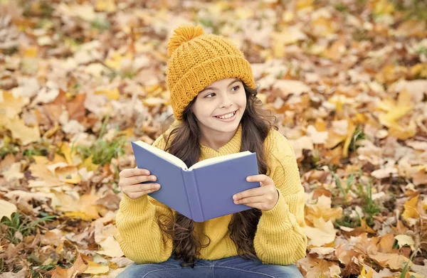 La connaissance est une semence qui grandit lorsque vous lisez. Un enfant heureux lit un livre assis sur des feuilles d'automne. Journée du savoir. Le 1er septembre. Enseignement primaire. Bibliothèque scolaire. Page par page pas besoin d'attendre — Photo