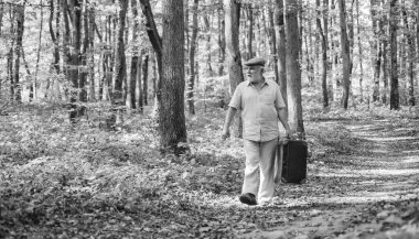 Seyahat ve tatil. Sonbahar sezonu. İdealist doğası. Yaşlı adam bavulla yürüyor. Emeklilik. Ormanda seyahat çantası taşıyan yaşlı bir adam. Kıdemli insan sonbahar ormanlarında seyahat eder. İyi yolculuklar.