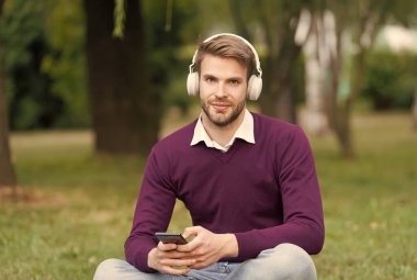 Gülümseyen genç yakışıklı adam parkta müzik dinliyor, modern hayatta teknoloji...