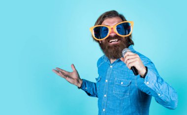 Mikrofonlu komik sakallı adam. Tıraşsız, uzun saçlı adam. Berber ve kuaför. Erkek mikrofonda şarkı söyler. kopyalama alanı. Parti gözlüklü vahşi beyaz hippi. karaoke şarkıcısı