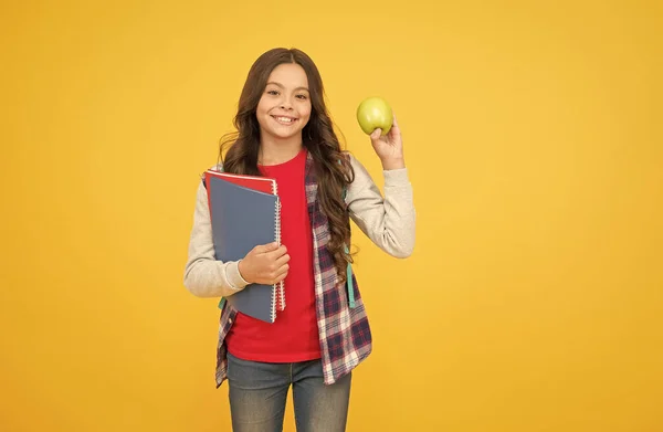 Mały dzieciak trzymać książki szkolne i naturalne jabłko żółte tło, zdrowe odżywianie — Zdjęcie stockowe