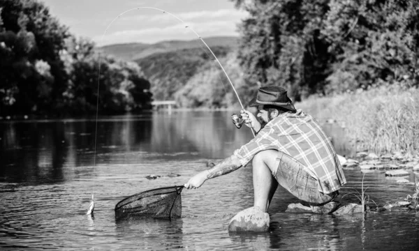 Lo pillo yo solo. hombre barbudo con pescado en caña. pesca hipster con cuchara-cebo. pasatiempo peces mosca. Hipster con camisa a cuadros. pescador exitoso en el agua del lago. pesca de caza mayor. relajarse en la naturaleza — Foto de Stock