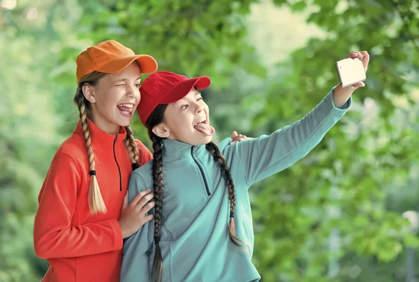 Ragazze allegre migliori amici. Indossa vestiti sportivi. ragazze adolescenti trascorrere del tempo insieme divertendosi. stile di vita infantile digitale. la convivenza. felice giorno dei bambini. i bambini fanno selfie con smartphone — Foto Stock