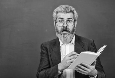 Ders kitabı olan bir öğretmen. Tecrübeli öğretmen. Uygun kurslar seçiliyor. Kitabı olan öğretmen konuyu açıklar. Kara tahtanın önündeki adam. Üniversite ve lise. Edebiyat konusu. Kitap okumak