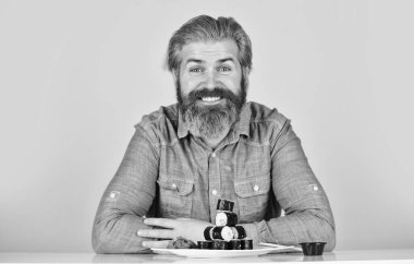 Japon yemek teslimatı. Suşi ruloları. Asya yemeği. Suşi siparişi. Adam evde suşi yiyor. Çubuklu suşi ve zencefil. Japon mutfağı. Doğu kültürü. Sakallı hippi börek yiyor.