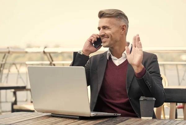 Felice uomo d'affari dare gesto di saluto mano parlando sul telefono cellulare in internet cafè all'aperto, saluto — Foto Stock