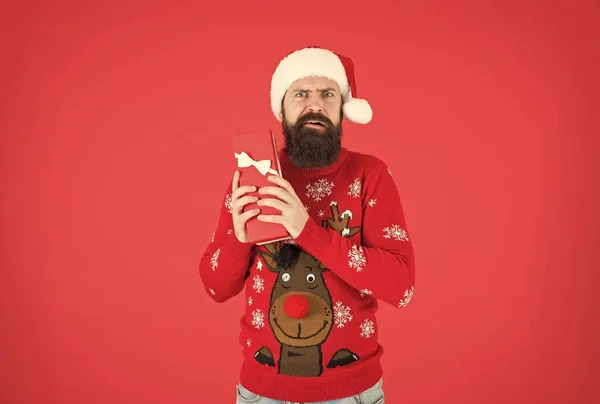 Ünnepeljük a téli ünnepeket. Boldog karácsonyt! Egy férfi vicces kötött pulóverben dobozzal. Karácsonyi bevásárlás. Készíts ajándékokat és ajándékokat. érdeklődő szakállas férfi télapó sapkában. Boldog új évet party szórakozás — Stock Fotó