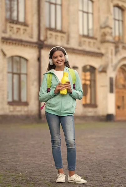 Hälsa återfuktning för barn med vattenflaska lyssna musik i hörlurar och bära skolan ryggsäck utomhus, sport och fitness — Stockfoto