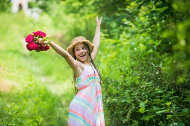 Hasır şapkalı mutlu bir kız ve yaz doğasında güller, mutluluk.