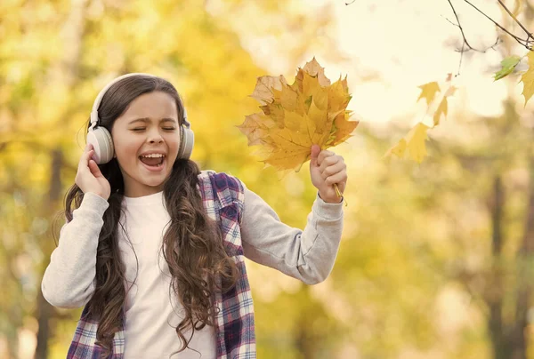 トレンディな美しさ。子供の頃の幸せ。美しさと自然。幸せな子供はヘッドフォンを着用する。10代の女の子は学校に行く途中で音楽を聴く。子供は秋の森を歩く。公園にもみじの葉が落ちる。オンライン教育 — ストック写真