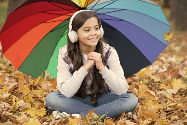 Ich fühle mich beschützt. Herbstkind unter buntem Regenschirm. Spüren Sie die Inspiration. glückliche Kindheit. zurück zur Schule. Mädchen im Kopfhörer im Park. Genießen Sie den Herbst im Wald. Musik hören. Online-Kurse — Stockfoto