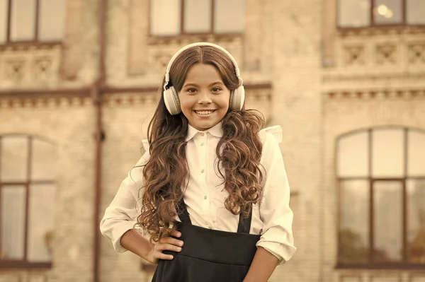 Colegiala feliz en uniforme elegante. felicidad infantil. niño en auriculares digitales. pequeña estudiante escuchar música al aire libre. de vuelta a la escuela. niña pequeña buscando inteligente e inteligente — Foto de Stock