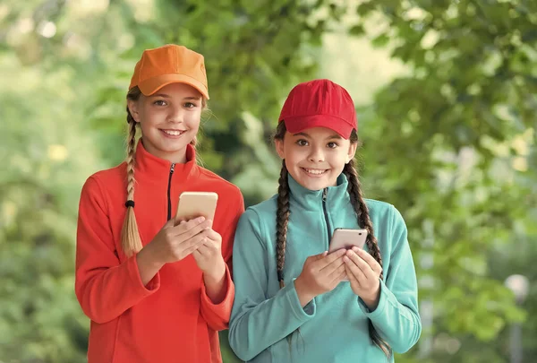 Retrato de hermanas felices con smartphone. Los niños pequeños se divierten. Dos chicas hipster sonrientes con ropa deportiva. niños despreocupados posando al aire libre. Modelos positivos. Traje casual hipsters — Foto de Stock