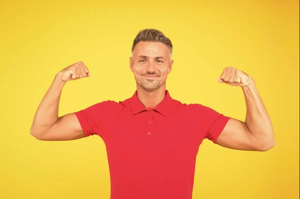 Homme athlétique fort sourire en t-shirt rouge fléchissant bras musclés fond jaune, la force — Photo