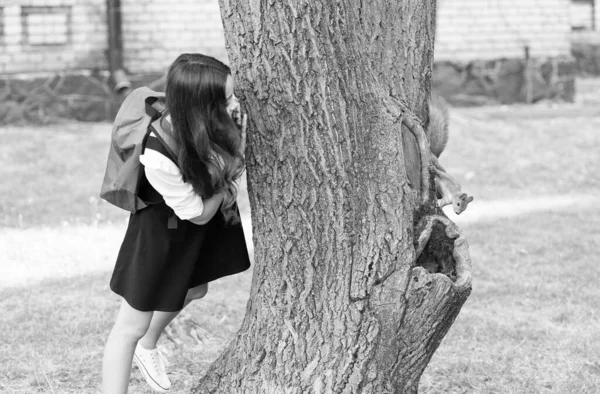 Studiować naturę, nie książki. Małe dziecko patrzy na wiewiórkę wspinającą się na pień drzewa. Zajęcia z przyrody w parku. Badania na zwierzętach. Edukacja ekologiczna. Nauka przyrodnicza. Zoologię. 1 września. Wracamy do szkoły. — Zdjęcie stockowe