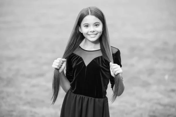 Glückliches kleines Mädchen mit Schönheitslook Lächeln hält lange brünette Haare in Modekleid grünes Gras sonnigen Sommer im Freien, Salon — Stockfoto