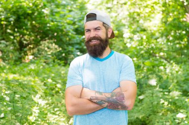 Sakallı, bıyıklı, yaz tişörtlü ve şapkalı olgun sakallı bir adam.