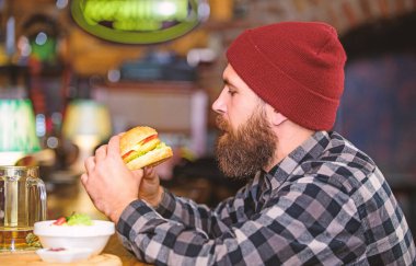 Bar rahatlamak ve içmek için rahatlatıcı bir yer. Sakallı adam bira içer hamburger menüsü yer. Barda afiyet olsun. Barda oturan vahşi hippi sakallı adam. Yüksek kalorili atıştırmalık. Hipster barda dinleniyor.