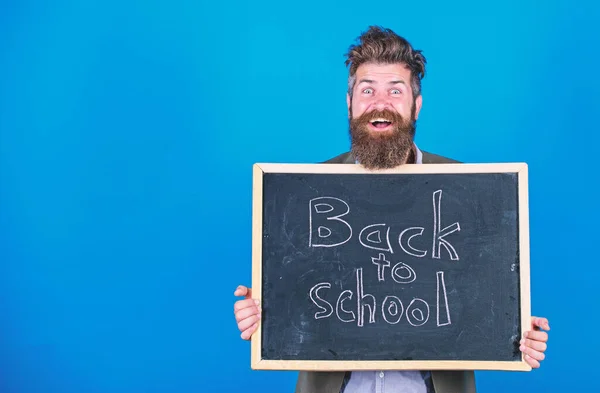 Tanár szakállas ember áll, és tartja tábla felirattal vissza az iskola kék háttér. A tanár felkéri, hogy folytassa a tanulást. Folytasd velünk az oktatást. Új szemeszter az iskolában — Stock Fotó
