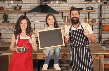 Anne, baba ve kız mutfakta karatahta, aşk konseptiyle yemek pişiriyorlar.