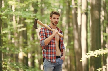 Modern oduncu. Çiftlik adamı baltayı taşır. Seksi adam ormanda düğmesiz gömlek giyer. Erkek gücü ve enerji. Kamp alanında yakacak odun. Kamp ve yürüyüş. Açık hava aktivitesi. Baltalı güçlü bir adam. Oduncu.