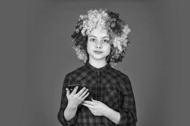 Küçük kız renkli peruk, akıllı telefon kullanıyor. Olumlu ve neşeli. çocukluk mutluluğu. Gökkuşağı peruğu saçlı çocuk komik görünüyor. Kuaförde saç boyama. Çocuk eğleniyor. Mutlu yıllar.