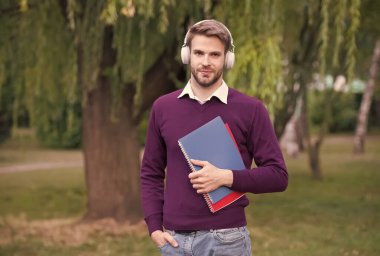 Kulaklıklı akıllı adam kitabı okurken müzik dinliyor. Adam not almak için defteri tutuyor. Faydalı bilgi almak. Adam okumayı seviyor. Öğrenci hayatı. kitaplı eğitim