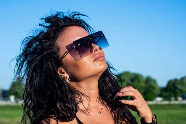 sexy brunette woman has long curly hair wearing stylish sunglasses and enjoy summer weather outdoor. fashion and beauty. fashionable girl in trendy glasses. Female enjoy the sun