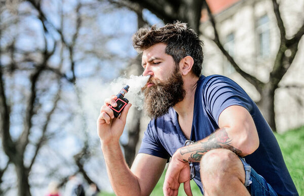 мужчина курит электронную сигарету. Зрелый хипстер с бородой. Хипстерский человек держит ваппинговый прибор. Бородатый жестокий мужчина курит электронную сигарету. Безопасность и зависимость от здоровья. Вдыхаю пар. Крепкий и мужественный