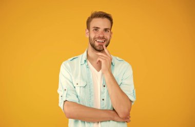 Havalı gülümseyen adam sarı arka planda rahat bir gömlek giyiyor, olumlu duygular içinde.