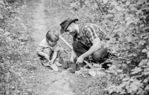 Boldog földi napot. Családi faiskola. Apa és fia cowboy kalapban a farmon. Kapa, edény és ásó. Kerti felszerelés. Öko farm. Kisfiú gyermek segít apának a gazdálkodásban. Kertészeti tevékenység — Stock Fotó