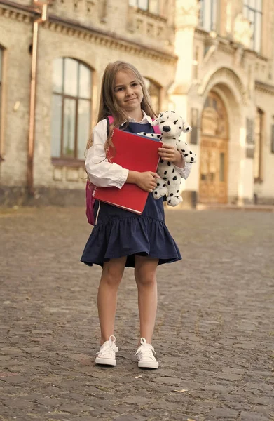 Förskoleutbildning. Förskolebarn utomhus. En liten unge håller i leksakshund och böcker. Lekskola och dagis. Eftermiddagsklubben. Att föra spelet till lärande — Stockfoto