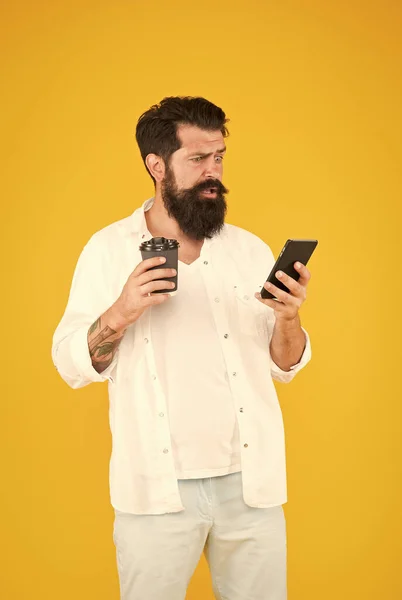 Şaşırmış sakallı ve bıyıklı adam cep telefonundan mesaj okuyor ve kahve fincanı tutuyor. Sürpriz. — Stok fotoğraf