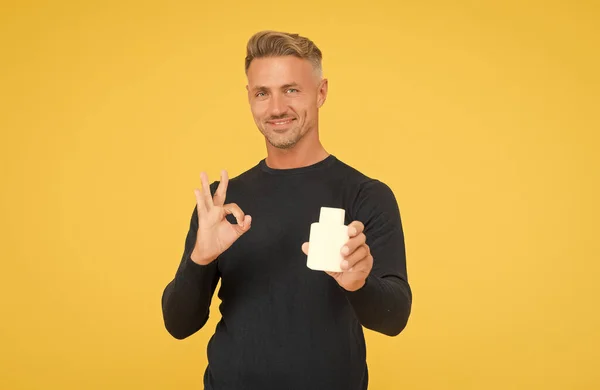 Feliz hombre guapo mostrar aprobación gesto de mano presentando producto cosmético fondo amarillo, OK — Foto de Stock