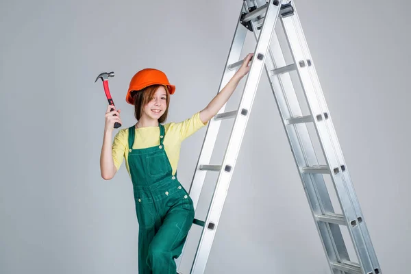 Adolescente lavoratrice in casco protettivo e uniforme su scala con martello, costrizione — Foto Stock