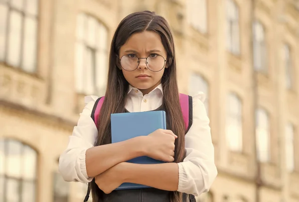 Petit enfant malheureux à lunettes tenir livre d'étude dans la cour d'école à l'extérieur, retour à l'école — Photo