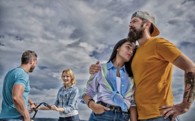 Kız arkadaşına bisiklet al. Bisiklet kirala ve eğlen. Bisiklet kiralama servisi konsepti. Çiftler boş zamanlarını gökyüzü arka planında geçirirler. Bisikletli çift harika vakit geçirirken diğer çift sıkılıyor.