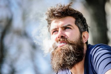 Sakallı adam. Sağlık güvenliği ve bağımlılık. Buhar soluyarak. Hipster adam buhar makinesi tutuyor. Sakallı, olgun bir hippi. Elektronik sigara içen bir adam. Elektronik sigara içen vahşi erkek sakallı.