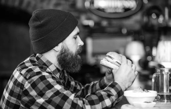 Bar rahatlamak ve içmek için rahatlatıcı bir yer. Sakallı adam bira içer hamburger menüsü yer. Barda afiyet olsun. Barda oturan vahşi hippi sakallı adam. Yüksek kalorili atıştırmalık. Hipster barda dinleniyor. — Stok fotoğraf