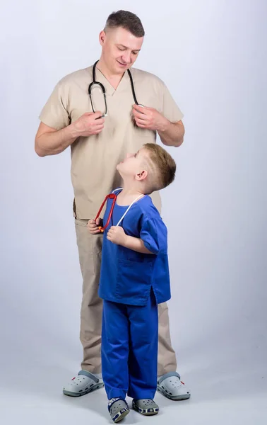 귀여운 아이가 의사 놀이를 한다. 가족 의사. 소아과 의사의 개념입니다. 청진기를 든 아버지와 작은 아들의 의사 복장이요. 의학 과 건강 관리. 미래의 직업. 아빠처럼 의사가 되고 싶어 — 스톡 사진