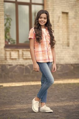 Uzun dalgalı saçlı mutlu bir kız çocuğu günlük moda tarzında şehir dışı modasına uygun giyinir.