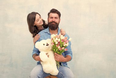 Baba-kız, bahar lale çiçeği buketi ve oyuncak ayıyla kucaklaşır. Babalar günü.