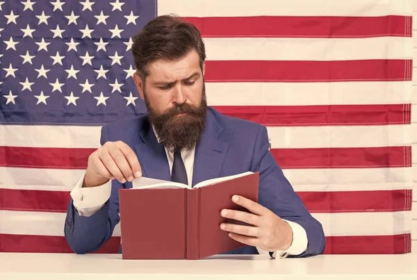 Anglicky. Americký bibliofil. Vousatý muž četl knihu na pozadí vlajky USA. Čtení a porozumění. Doma. Samostatná lekce. Škola a vzdělání. Vylepšete své schopnosti čtení — Stock fotografie